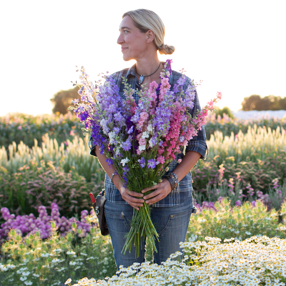 Erin Benzakein standing in the field holding a handful of larkspur