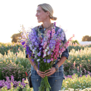 Erin Benzakein standing in the field holding a handful of larkspur