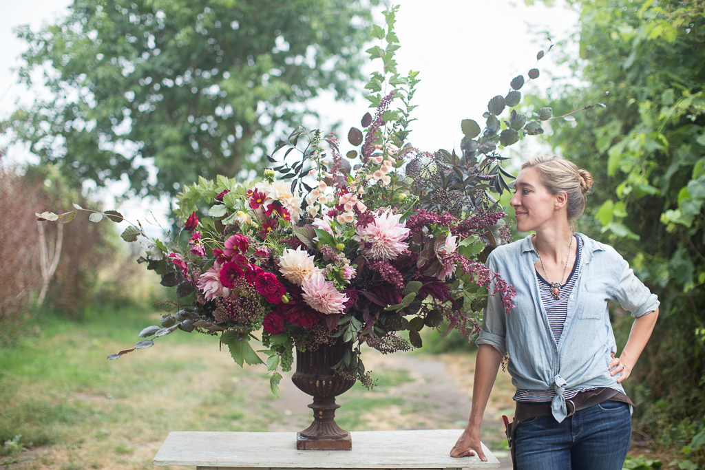 Erin Benzakein smiling at a beautiful large-scale flower arrangement she created