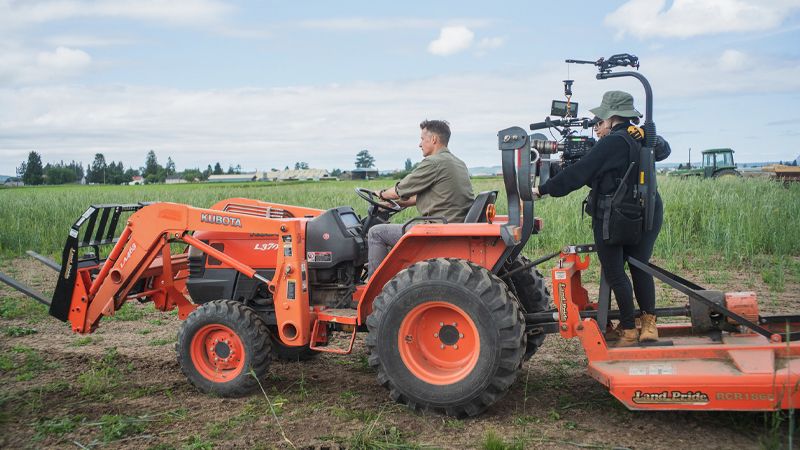 Chris Benzakein driving a tractor with a film crew in the back on a trailer